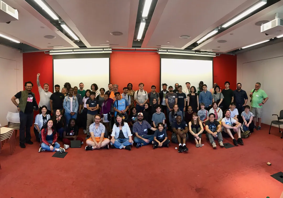 A group photograph at NYU MAGNET, with everyone gathered in front of a red wall.